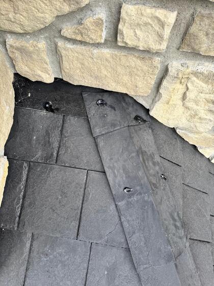 black sealant used to seal fasteners on a black rubber shingle where it meets the wall sided with masonry